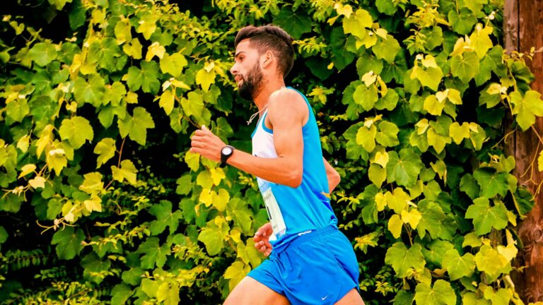 A man jogging outdoors beside vibrant green leaves, embodying fitness and energy.