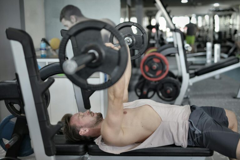 A young man performs a bench press exercise with a barbell in a modern gym environment.
